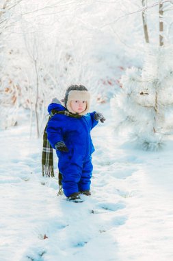 Kışın kar ile çocuk parkta. Mavi tulum içinde küçük bir çocuk ve bir örgü şapka, Noel'de kar taneleri bir kış parkta yakalar. Karla kaplı ormanda çocuk oyun