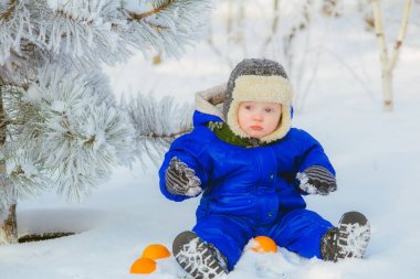 Kışın kar ile çocuk parkta. Mavi tulum içinde küçük bir çocuk ve bir örgü şapka, Noel'de kar taneleri bir kış parkta yakalar. Karla kaplı ormanda çocuk oyun