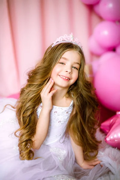女孩与金发长发粉红色的礼服公主和皇冠上的气球周围 — 图库照片