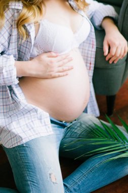 Genç güzel hamile kadın mavi kot pantolon ve hafif bir gömlek. Onun elinde yeşil bir fern bir dalı olan hamile kadın. Eko yaşam tarzı