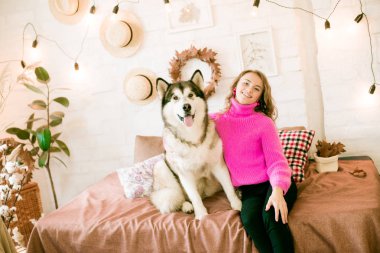 Evde sarı kıvırcık saçlı tatlı bir genç kız. Çatı katındaki yatakta, kocaman bir köpeğiyle. İnsanlar ve Köpekler.