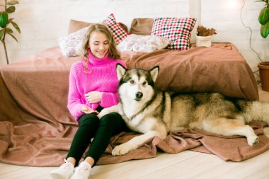 Evde sarı kıvırcık saçlı tatlı bir genç kız. Çatı katındaki yatakta, kocaman bir köpeğiyle. İnsanlar ve Köpekler.