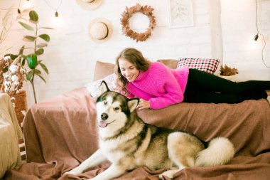 Evde sarı kıvırcık saçlı tatlı bir genç kız. Çatı katındaki yatakta, kocaman bir köpeğiyle. İnsanlar ve Köpekler.