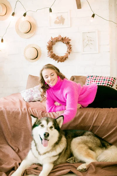 自宅で金髪の巻き毛を持つかわいい十代の女の子 大きなMalamute犬とロフトのベッドの上に 人と犬 — ストック写真