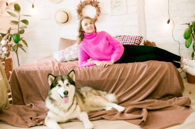 Evde sarı kıvırcık saçlı tatlı bir genç kız. Çatı katındaki yatakta, kocaman bir köpeğiyle. İnsanlar ve Köpekler.