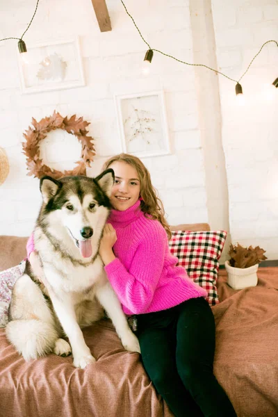 Evde sarı kıvırcık saçlı tatlı bir genç kız. Çatı katındaki yatakta, kocaman bir köpeğiyle. İnsanlar ve Köpekler.