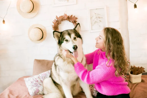 Evde sarı kıvırcık saçlı tatlı bir genç kız. Çatı katındaki yatakta, kocaman bir köpeğiyle. İnsanlar ve Köpekler.
