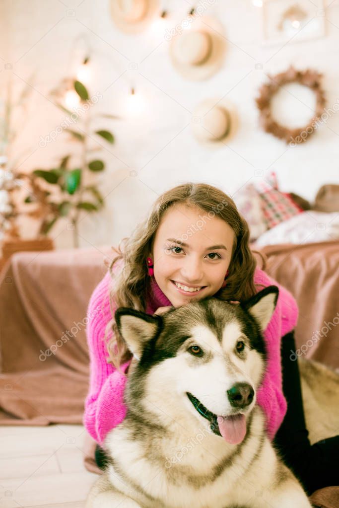 Cute teenage girl with blond curly hair at home, on the bed in the loft with a big malamute dog. People and Dogs.