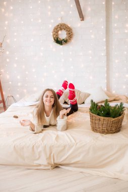 Sevimli bir genç kız, evinde, yatağın üzerinde, çelenk ve iğnelerle süslenmiş bir çatı katında eğleniyor. Noel havası