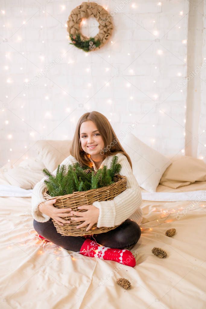 Cute teenage girl has fun at home in a light loft on the bed, decorated for Christmas with garlands and needles. Christmas mood
