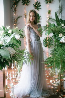 Sarışın ve akşam makyajlı çekici genç kız tropik yeşillikler, beyaz orkideler, güller ve zambaklar arasında romantik bir elbise giyiyor. Güzellik ve moda