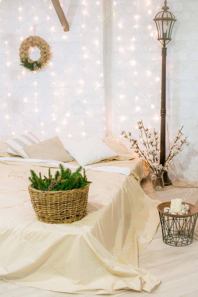 Bright bedroom with a large bright bed, in a loft style decorated with garlands and baskets with needles and cotton branches. New Year 2020. Christmas mood