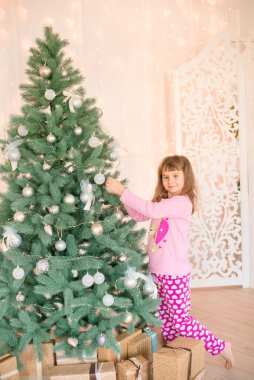 Noel ağacının yanında, üzerinde hediyeler, çelenkler, iğneler ve mumlarla süslenmiş parlak bir şömine olan pijamalı küçük şirin bir kız. Mutlu noeller. Noel havası