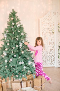 Noel ağacının yanında, üzerinde hediyeler, çelenkler, iğneler ve mumlarla süslenmiş parlak bir şömine olan pijamalı küçük şirin bir kız. Mutlu noeller. Noel havası