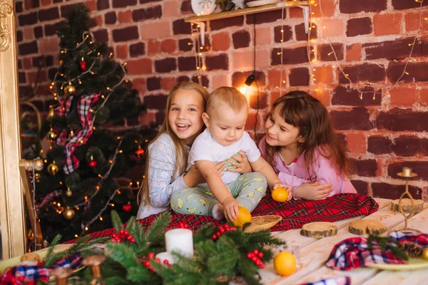 可爱的姐姐们和穿着睡衣的小兄弟们 在厨房的桌子边 一边吃着姜饼 一边在家里用圣诞花环和针头装饰着橘子 圣诞气氛 — 图库照片