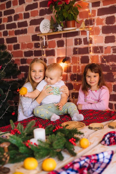 可爱的姐姐们和穿着睡衣的小兄弟们 在厨房的桌子边 一边吃着姜饼 一边在家里用圣诞花环和针头装饰着橘子 圣诞气氛 — 图库照片