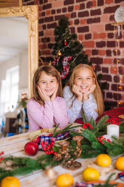 穿着睡衣的漂亮姐姐们在厨房的桌子旁边玩得很开心 桌上有姜饼饼干 家里有橘子 房间里装饰着圣诞花环和针头 圣诞气氛 — 图库照片