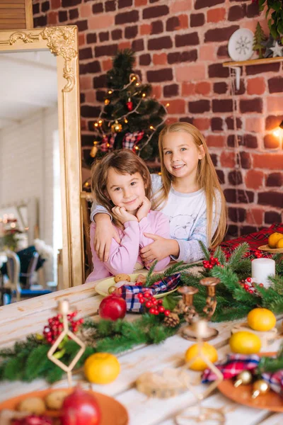 穿着睡衣的漂亮姐姐们在厨房的桌子旁边玩得很开心 桌上有姜饼饼干 家里有橘子 房间里装饰着圣诞花环和针头 圣诞气氛 — 图库照片