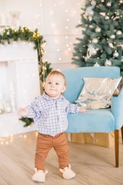 Noel ağacı ve çelenk ve hediyelerle süslenmiş şöminenin yanında tatlı bir çocuk. Noel havası