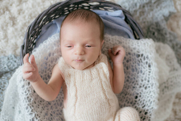 Cute little baby lies at home on a white fluffy carpet in a wicker basket with soft knitted plaids. Happy motherhood