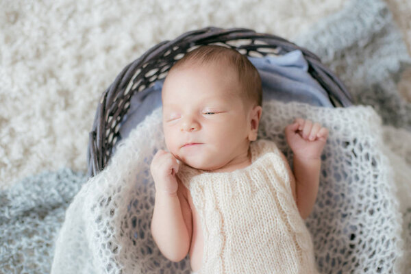 Cute little baby lies at home on a white fluffy carpet in a wicker basket with soft knitted plaids. Happy motherhood