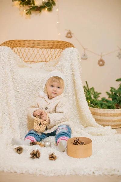 穿着白色针织毛衣的可爱小女孩坐在房间里的白色格子布上 房间里装饰着圣诞装饰品 壁炉上放着花环和针头 圣诞气氛 — 图库照片