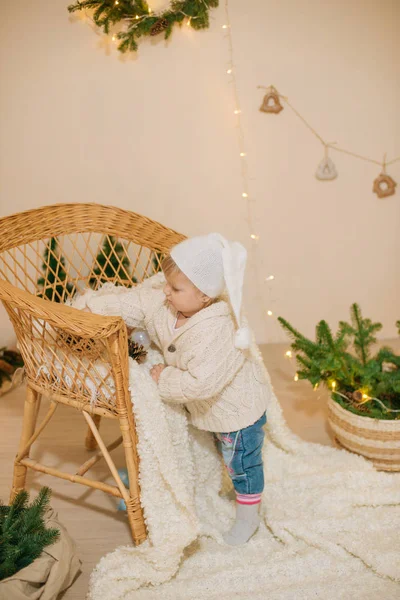 穿着白色针织毛衣的可爱小女孩坐在房间里的白色格子布上 房间里装饰着圣诞装饰品 壁炉上放着花环和针头 圣诞气氛 — 图库照片