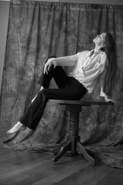 Beyaz tişörtlü, siyah pantolonlu, uzun saçlı ve tekstil arka planında stüdyoda poz veren güzel bir manken. Güzellik ve moda.