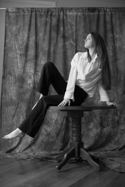 Beyaz tişörtlü, siyah pantolonlu, uzun saçlı ve tekstil arka planında stüdyoda poz veren güzel bir manken. Güzellik ve moda.