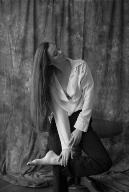 Beyaz tişörtlü, siyah pantolonlu, uzun saçlı ve tekstil arka planında stüdyoda poz veren güzel bir manken. Güzellik ve moda.