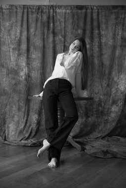 Beyaz tişörtlü, siyah pantolonlu, uzun saçlı ve tekstil arka planında stüdyoda poz veren güzel bir manken. Güzellik ve moda.