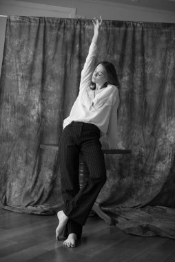 Beyaz tişörtlü, siyah pantolonlu, uzun saçlı ve tekstil arka planında stüdyoda poz veren güzel bir manken. Güzellik ve moda.