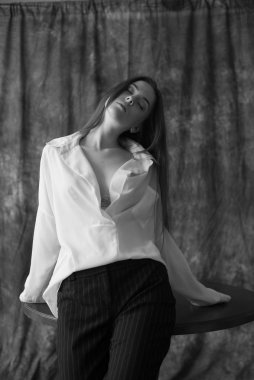 Beyaz tişörtlü, siyah pantolonlu, uzun saçlı ve tekstil arka planında stüdyoda poz veren güzel bir manken. Güzellik ve moda.