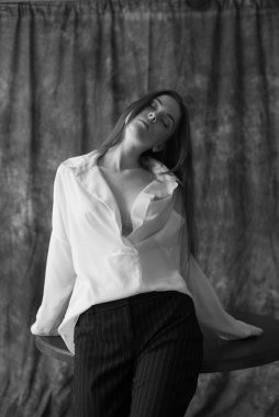 Beyaz tişörtlü, siyah pantolonlu, uzun saçlı ve tekstil arka planında stüdyoda poz veren güzel bir manken. Güzellik ve moda.