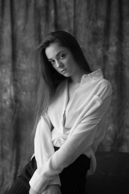 Beyaz tişörtlü, siyah pantolonlu, uzun saçlı ve tekstil arka planında stüdyoda poz veren güzel bir manken. Güzellik ve moda.