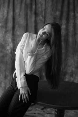 Beyaz tişörtlü, siyah pantolonlu, uzun saçlı ve tekstil arka planında stüdyoda poz veren güzel bir manken. Güzellik ve moda.