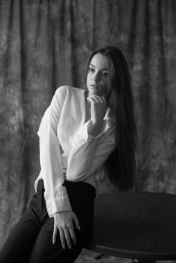 Beyaz tişörtlü, siyah pantolonlu, uzun saçlı ve tekstil arka planında stüdyoda poz veren güzel bir manken. Güzellik ve moda.