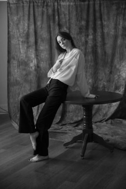 Beyaz tişörtlü, siyah pantolonlu, uzun saçlı ve tekstil arka planında stüdyoda poz veren güzel bir manken. Güzellik ve moda.