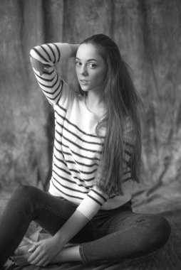 Çizgili kazaklı ve dar kotlu koyu renk uzun saçlı güzel bir manken stüdyoda tekstil arka planında poz veriyor. Güzellik ve moda.