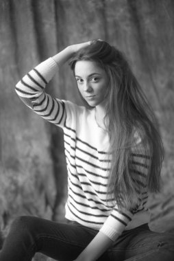 Çizgili kazaklı ve dar kotlu koyu renk uzun saçlı güzel bir manken stüdyoda tekstil arka planında poz veriyor. Güzellik ve moda.