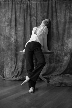 Beyaz tişörtlü, siyah pantolonlu, uzun saçlı ve tekstil arka planında stüdyoda poz veren güzel bir manken. Güzellik ve moda.