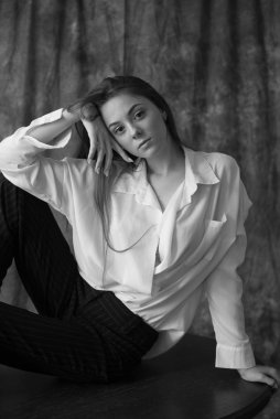 Beyaz tişörtlü, siyah pantolonlu, uzun saçlı ve tekstil arka planında stüdyoda poz veren güzel bir manken. Güzellik ve moda.