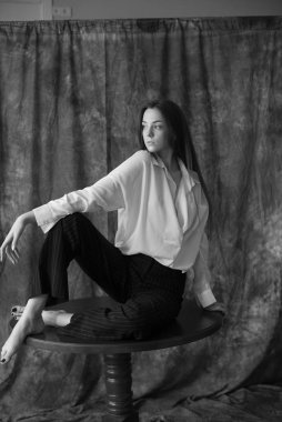 Beyaz tişörtlü, siyah pantolonlu, uzun saçlı ve tekstil arka planında stüdyoda poz veren güzel bir manken. Güzellik ve moda.