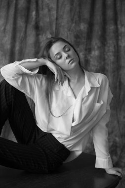 Beyaz tişörtlü, siyah pantolonlu, uzun saçlı ve tekstil arka planında stüdyoda poz veren güzel bir manken. Güzellik ve moda.