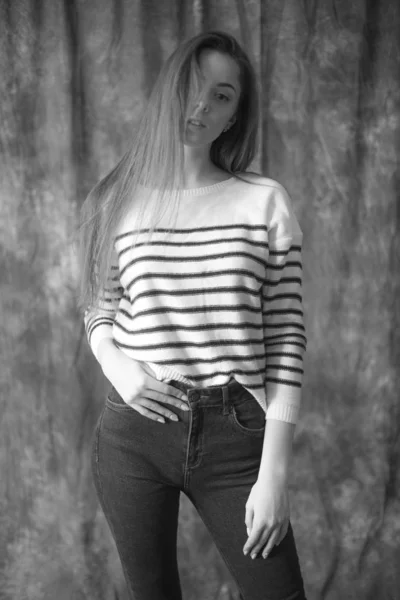 縞模様のセーターとスキニージーンズで黒い長い髪を持つ素敵な若い女の子モデルは 織物の背景にスタジオでポーズをとっています 美とファッション — ストック写真