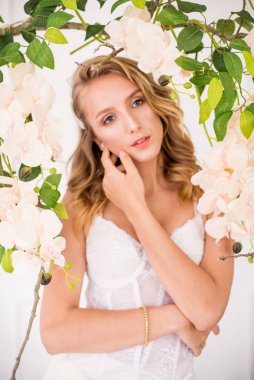 Sarışın, kıvırcık saçlı, güzel makyajlı, yumuşak dantelli, beyaz orkideli çekici bir genç kız.