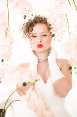 Beyaz orkideli, hafif bahar stüdyosunda beyaz elbiseli çekici bir gelin. Güzellik ve Moda