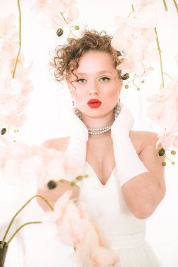 Beyaz orkideli, hafif bahar stüdyosunda beyaz elbiseli çekici bir gelin. Güzellik ve Moda