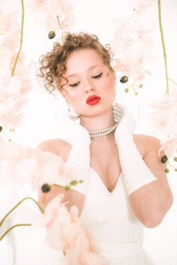 Beyaz orkideli, hafif bahar stüdyosunda beyaz elbiseli çekici bir gelin. Güzellik ve Moda