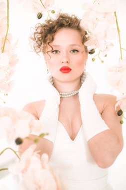 Beyaz orkideli, hafif bahar stüdyosunda beyaz elbiseli çekici bir gelin. Güzellik ve Moda